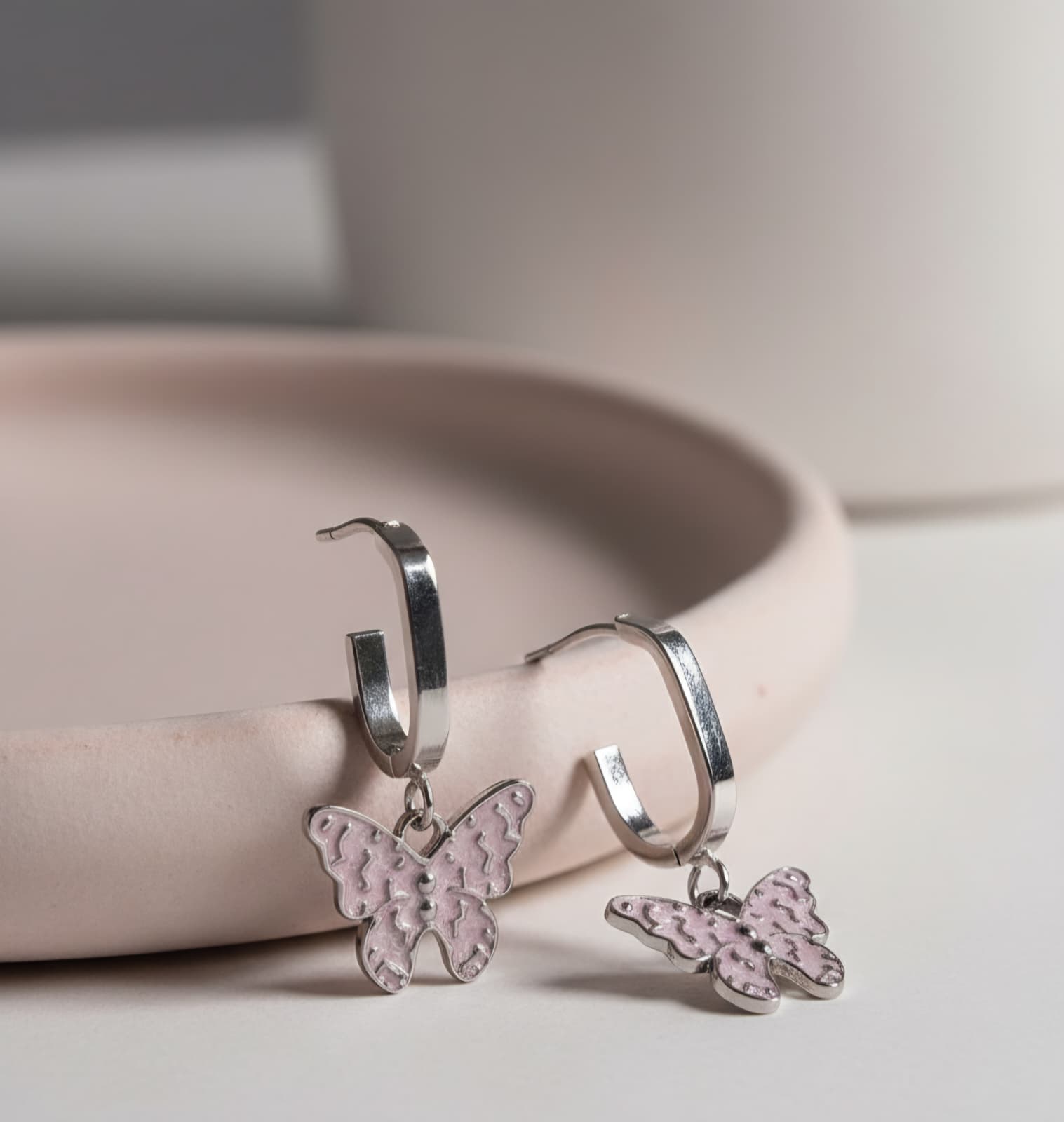 Silver hoop earrings with pink butterfly charms on a light surface.