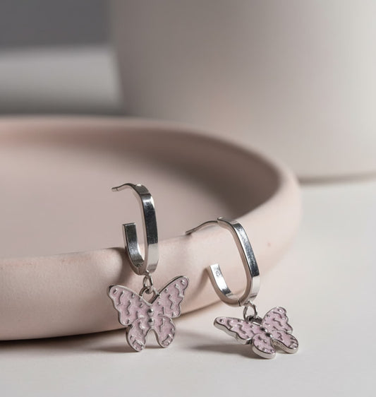 Silver hoop earrings with pink butterfly charms on a light surface.