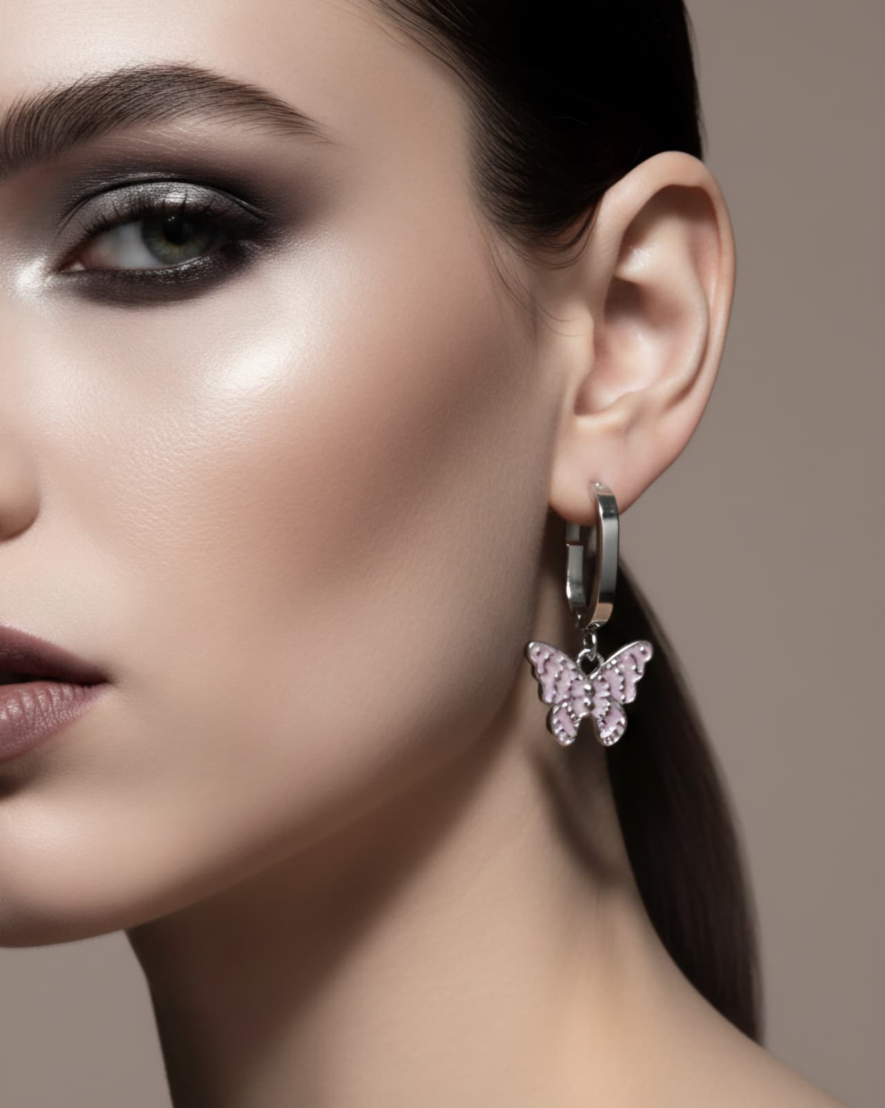 Close-up of a woman wearing butterfly earrings with a neutral background