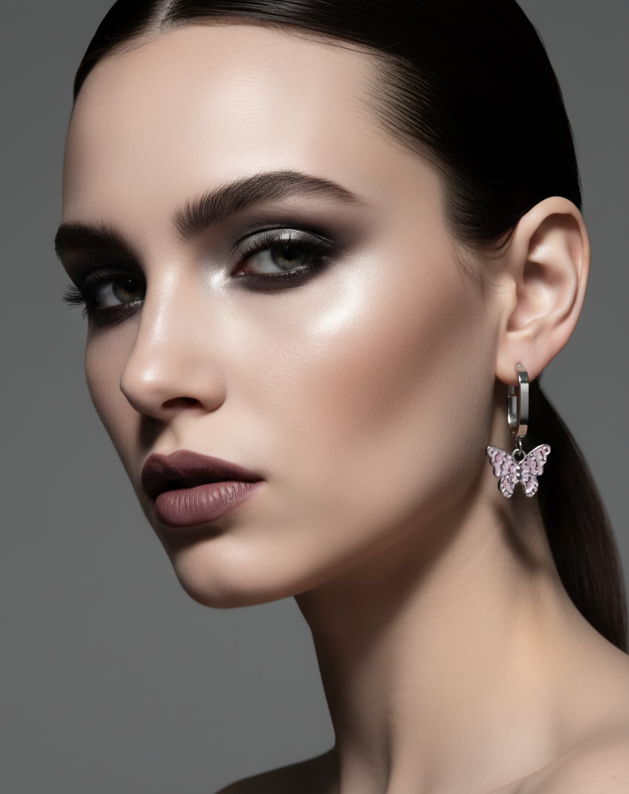Close-up of a woman wearing a butterfly earring against a gray background