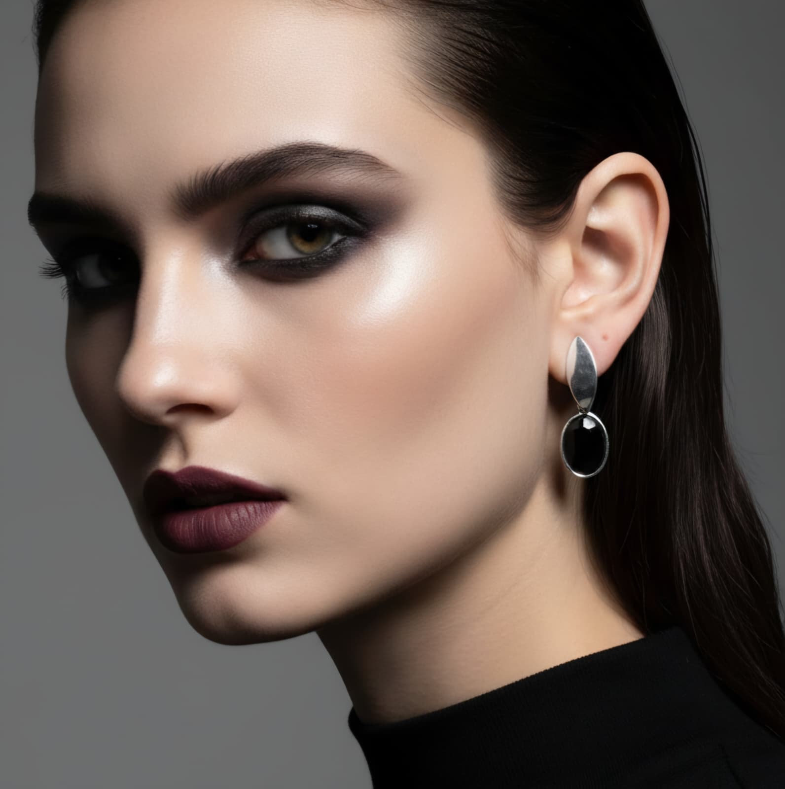 Close-up of a woman wearing a black earring against a gray background