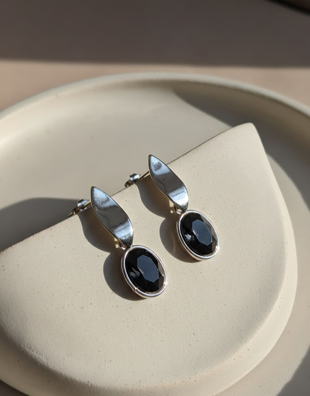 Pair of silver earrings with black stones on a beige plate