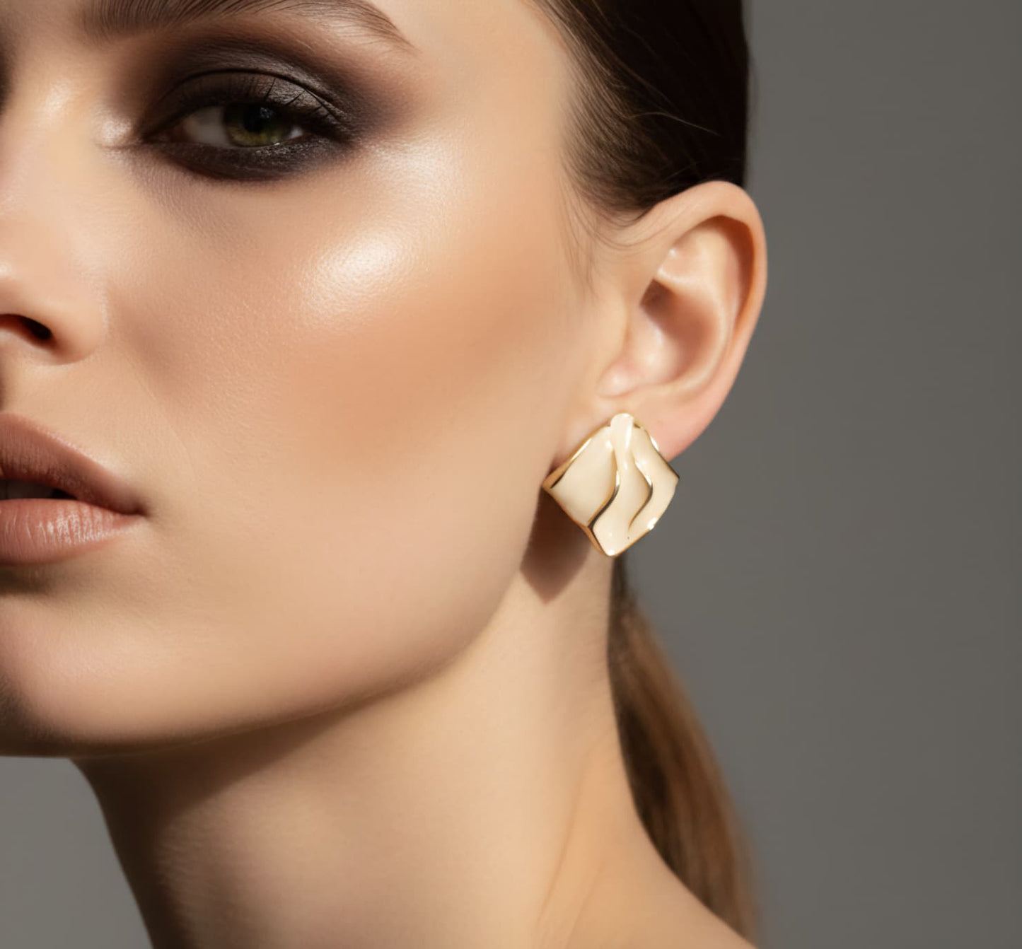 Close-up of a woman wearing gold earrings with a neutral background