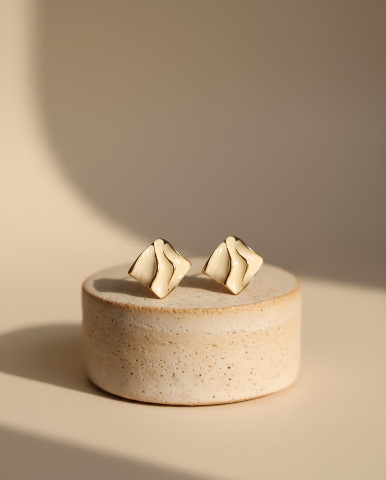 Gold earrings on a round beige stone surface with a soft beige background