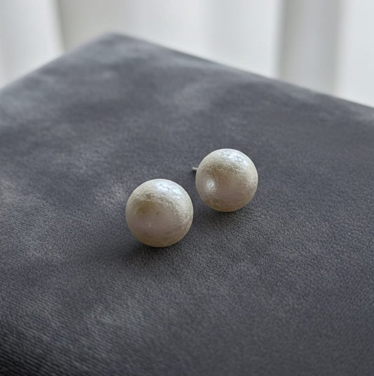 Pair of pearl stud earrings on a gray surface