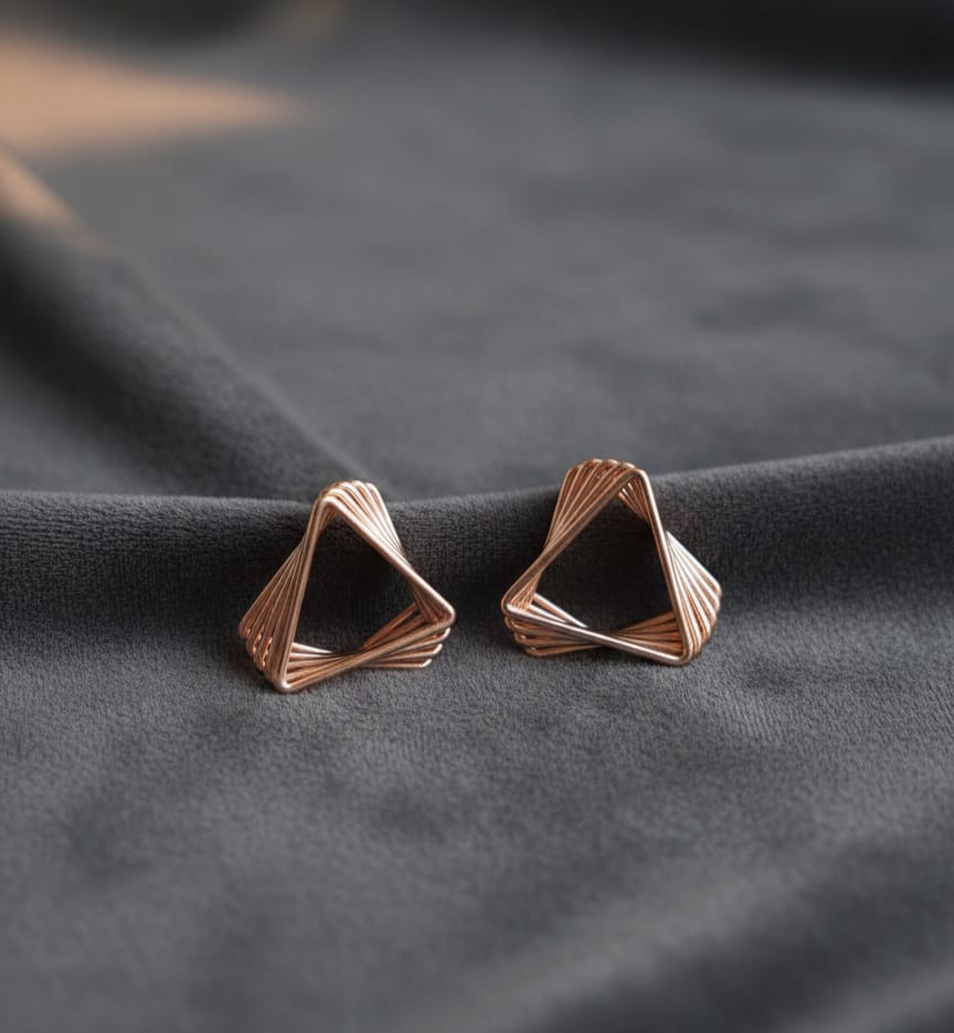 Rose gold geometric earrings on a dark fabric background