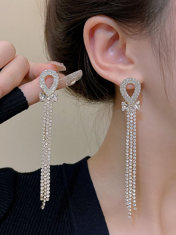 Silver earrings with dangling chains worn by a person against a neutral background
