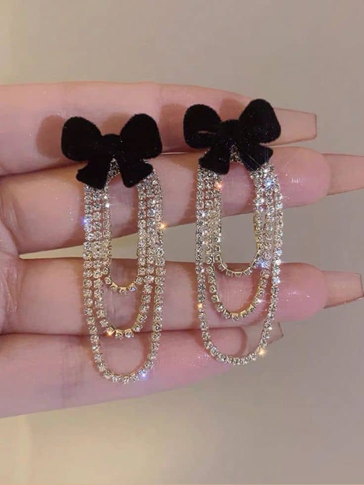 Hair clips with black bows and rhinestone chains held between fingers against a neutral background