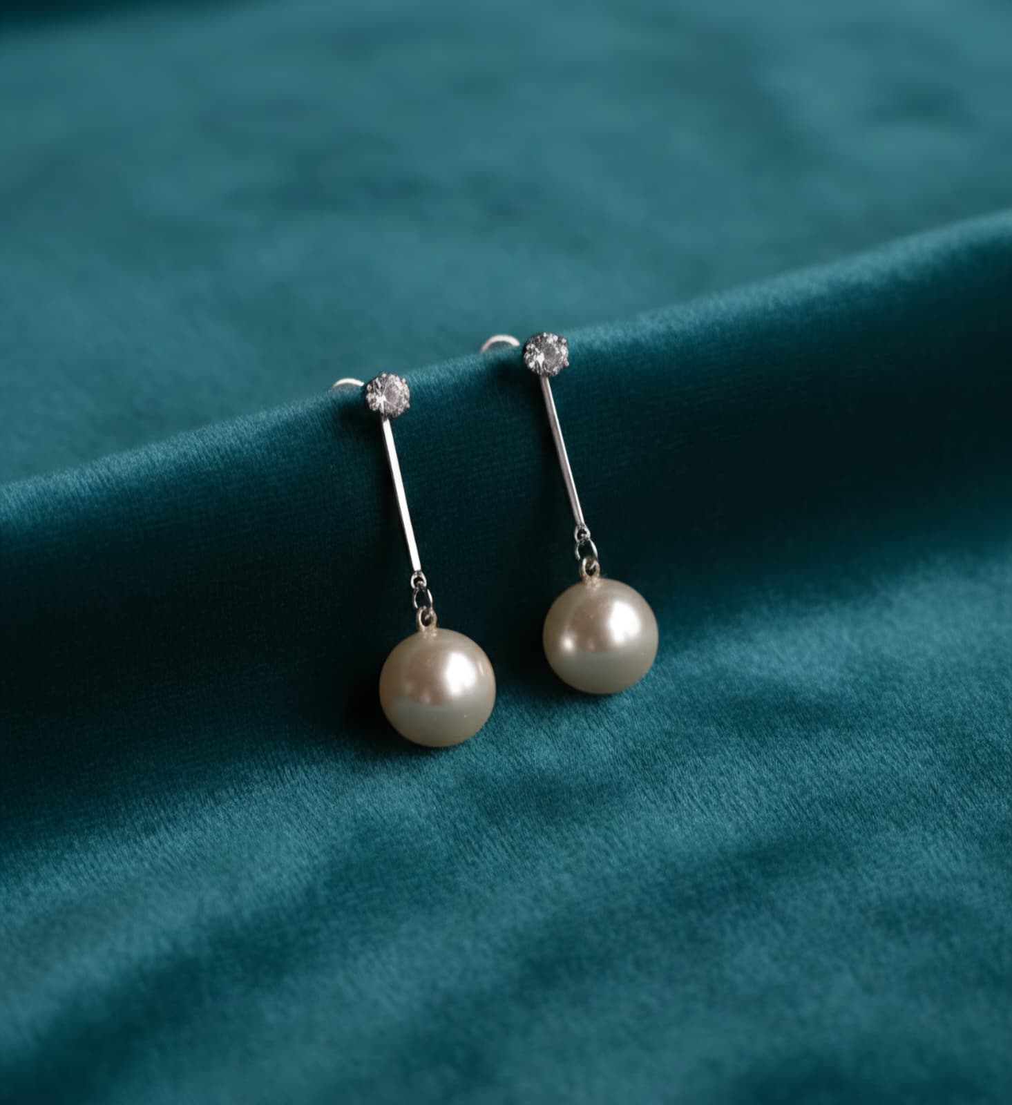 Pearl earrings on a teal fabric background